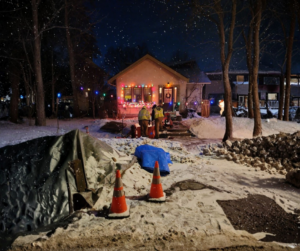 One-hole sewer repair in a Minneapolis yard during winter with snow and safety cones visible